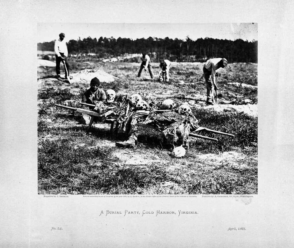 Gravediggers are in the process of digging into the earth with shovels. The front of the image features a man seated next to various skulls and bones belonging to Civil War soldiers. Behind him are four men in various states of digging into the ground.